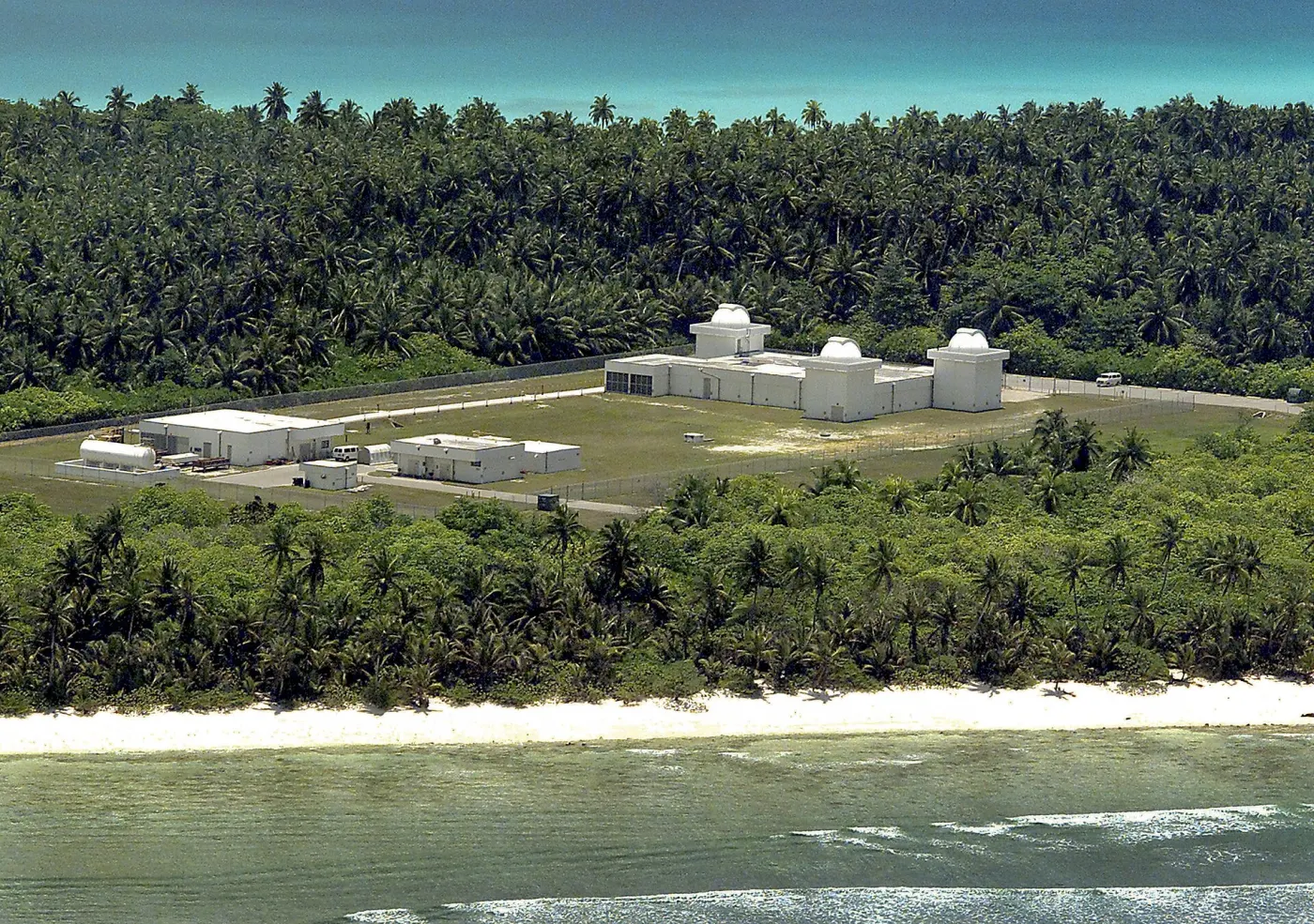 White telescope domes of the GEODSS site on Diego Garcia, surrounded by palm trees